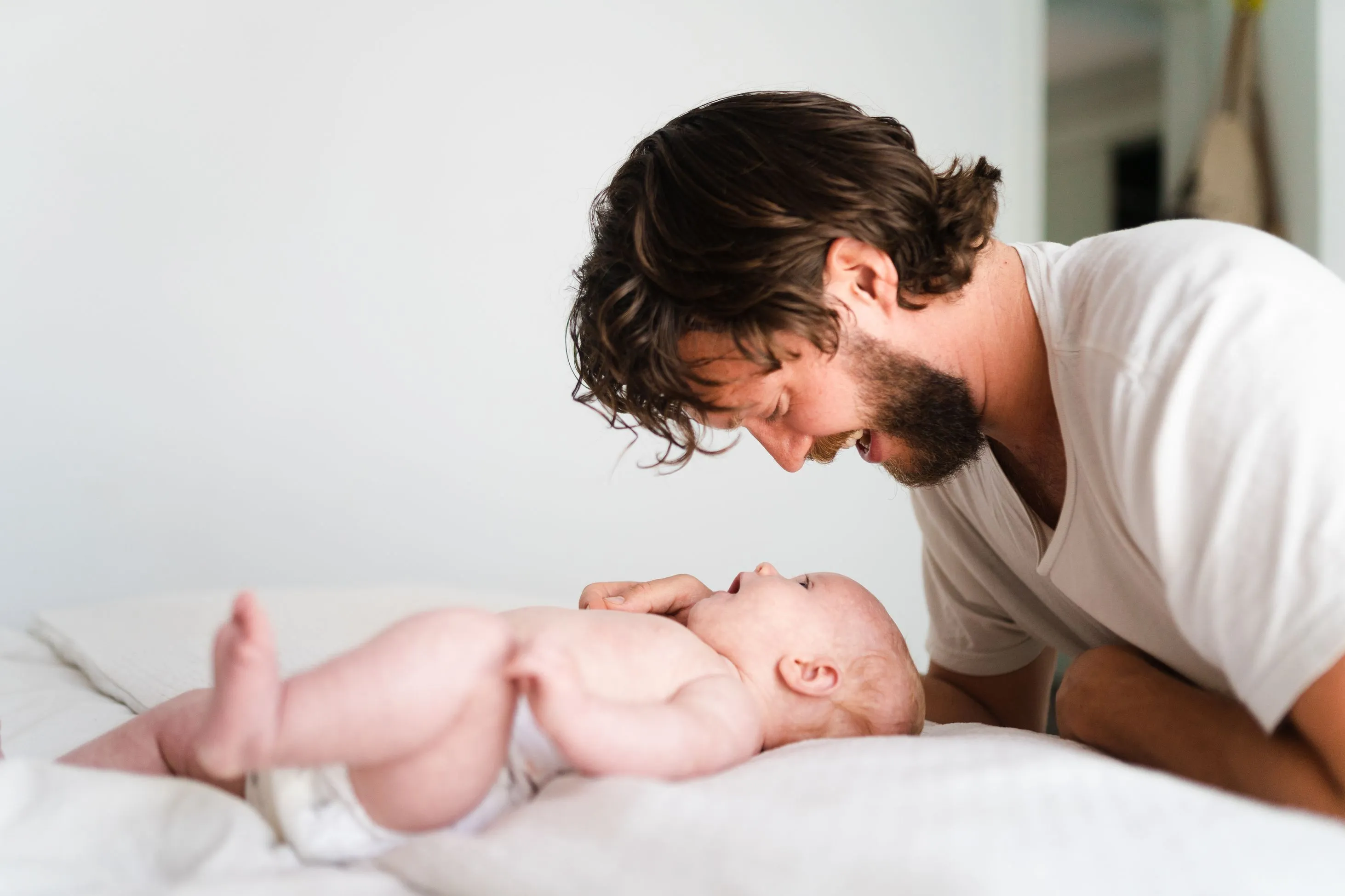 A father gently lays beside his baby on a bed.