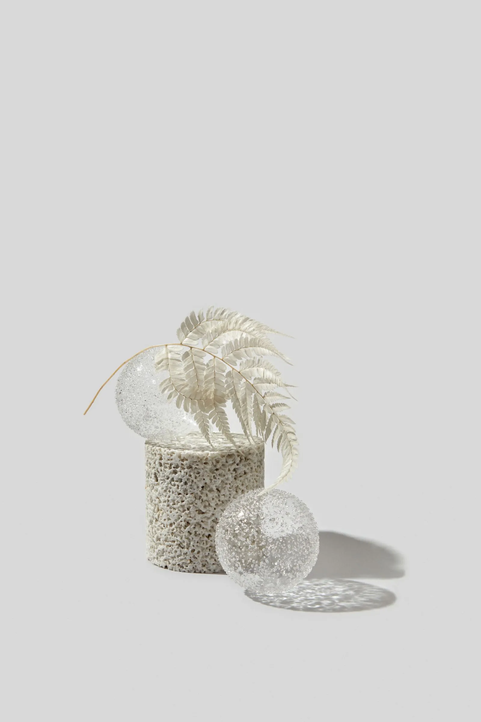 A simple white vase with a leaf resting inside, accompanied by a collection of small, polished stones